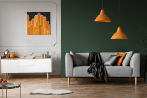 Orange lamps above grey couch in black living room interior with poster above cabinet. Real photo
